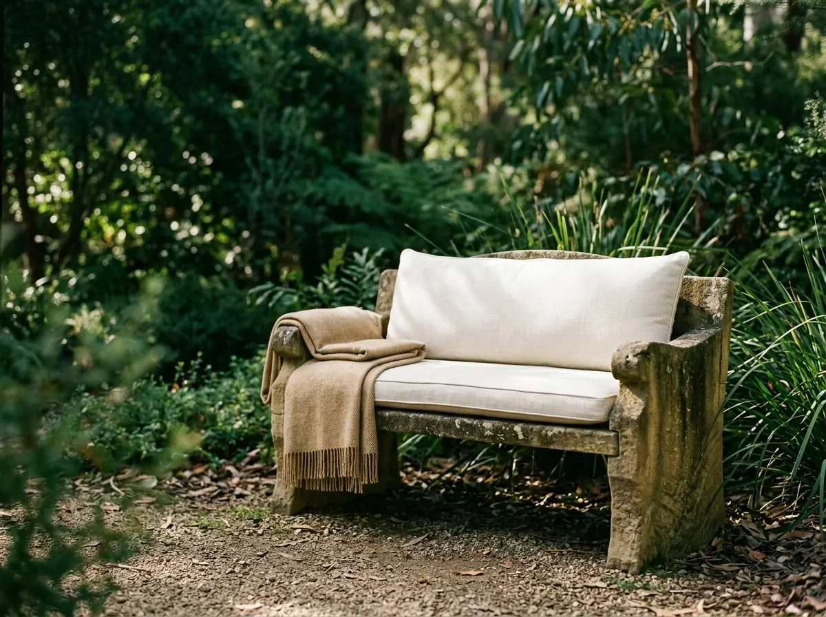 A sandstone garden bench with a linen cushion in dappled light